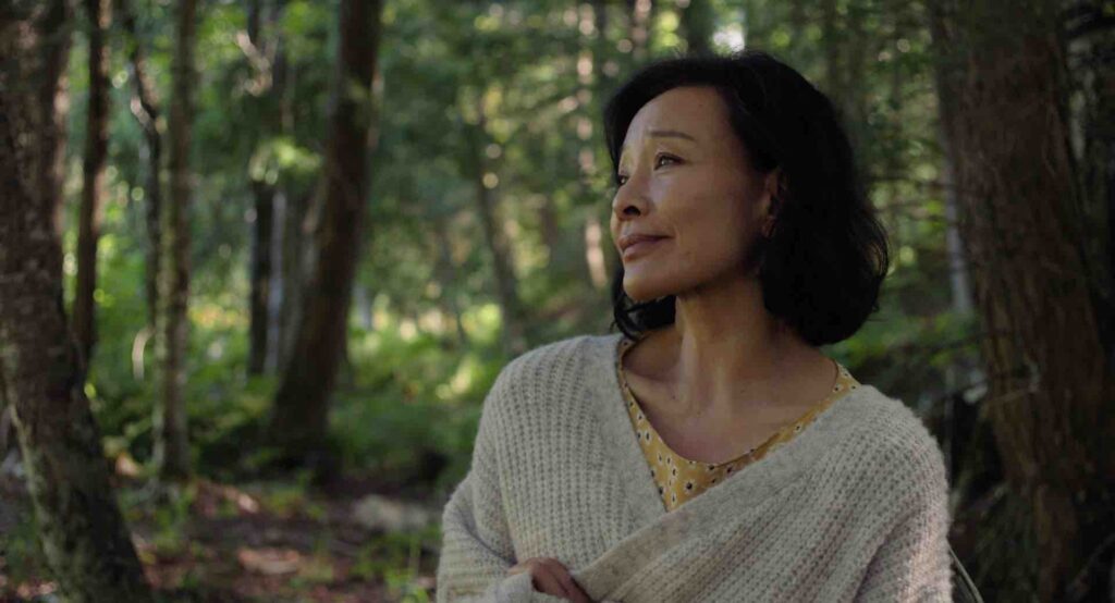 An Asian woman looking to the left holding onto her grey cardigan