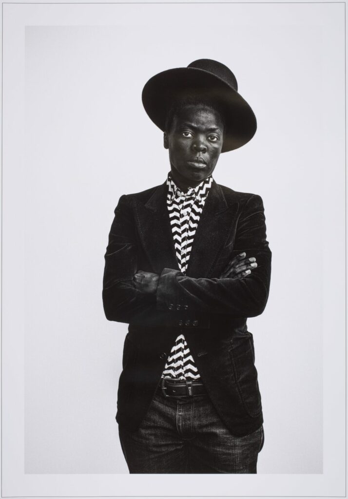 Muholi in black hat and jacket and black and white shirt with arms folded - &lsquo;Muholi Muholi&rsquo; Zanele Muholi South Africa, 2016 Courtesy of Bristol Museums & Archives&rdquo;
