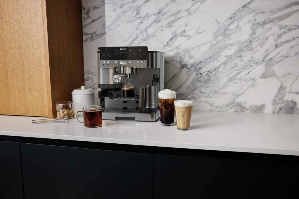 Ninja Luxe Café Premier coffee machine on a kitchen worktop with three prepared drinks beside it.