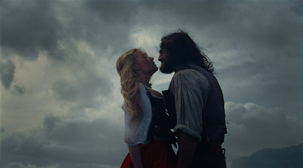 Margot Robbie and Jacob Elordi in s still from "Wuthering Heights" in period costume embracing on a moor (Image: Courtesy Warner Bros. Pictures.)