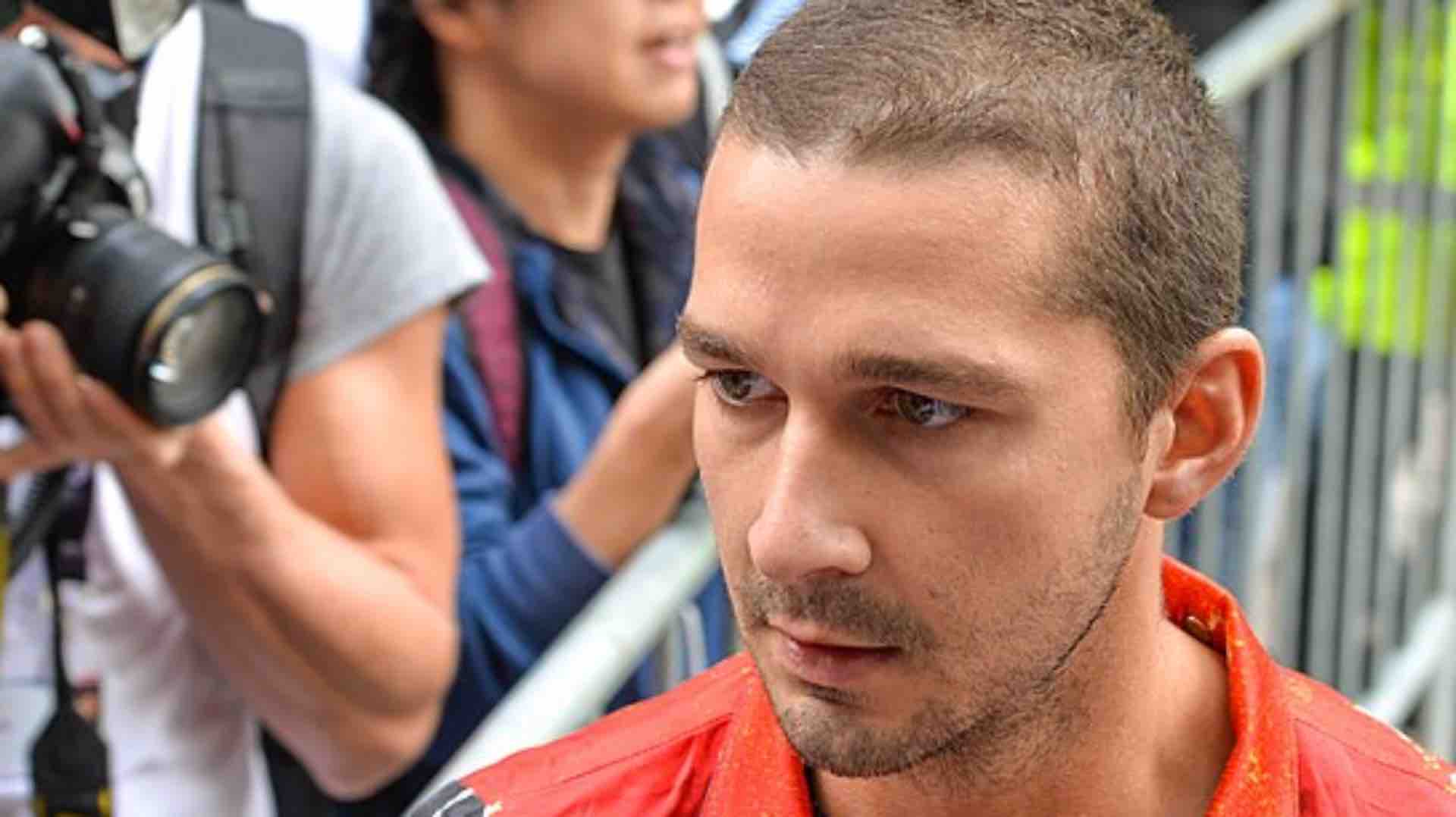 Shia LaBeouf in an orange shirt frowning