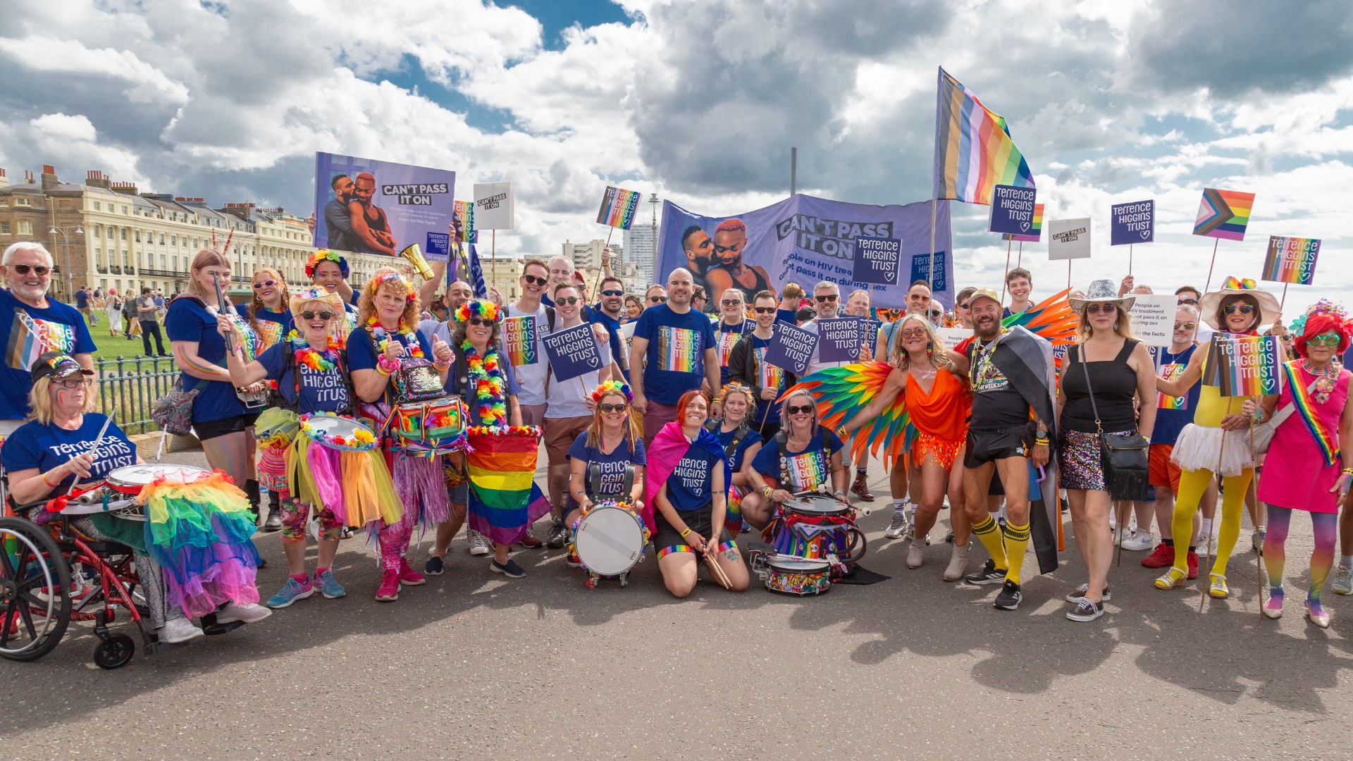 Team THT at Brighton Pride in 2025 – a large group standing and posing with rainbow flags and placards under a cloudy sky