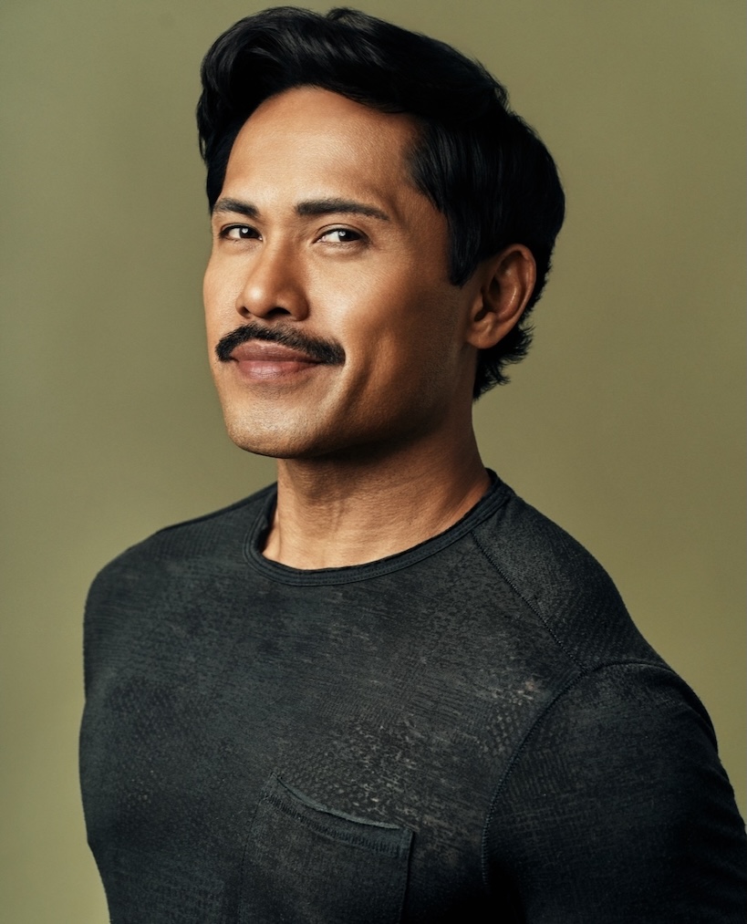 Joel Relampagos smirking in a black t-shirt, with a green background