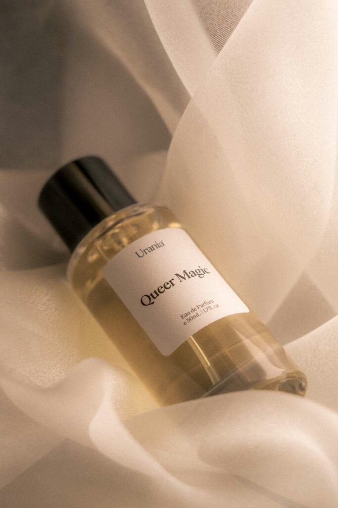 Bottle of Urania ‘Queer Magic’ perfume resting on soft, light-coloured fabric.