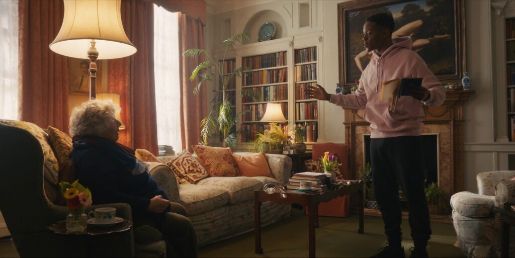 a still from the film showing Miriam sat down and Alistair stood up reading a book, sat in her front room
