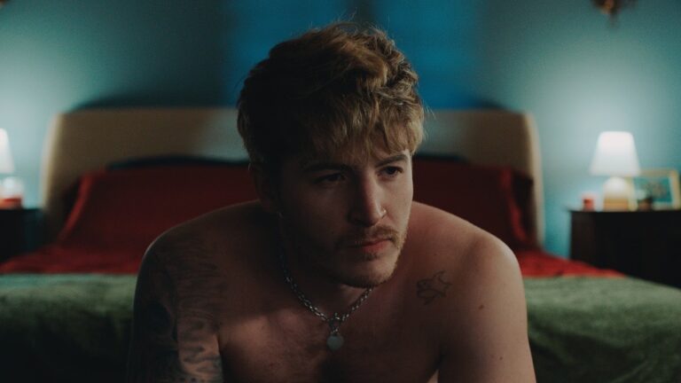 Kieron Moore sitting on a bed topless in a still from Blue Film