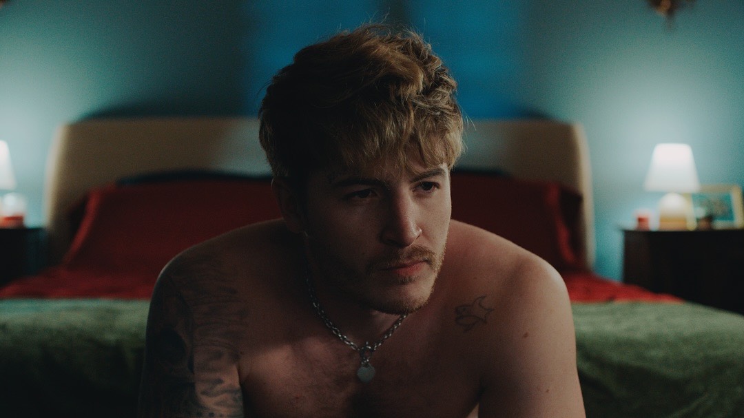 Kieron Moore sitting on a bed topless in a still from Blue Film