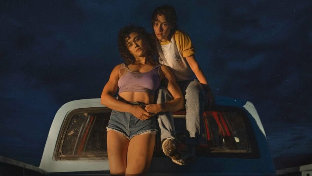 the main characters from Love Lies Bleeding sitting on a car and looking at the camera, nighttime