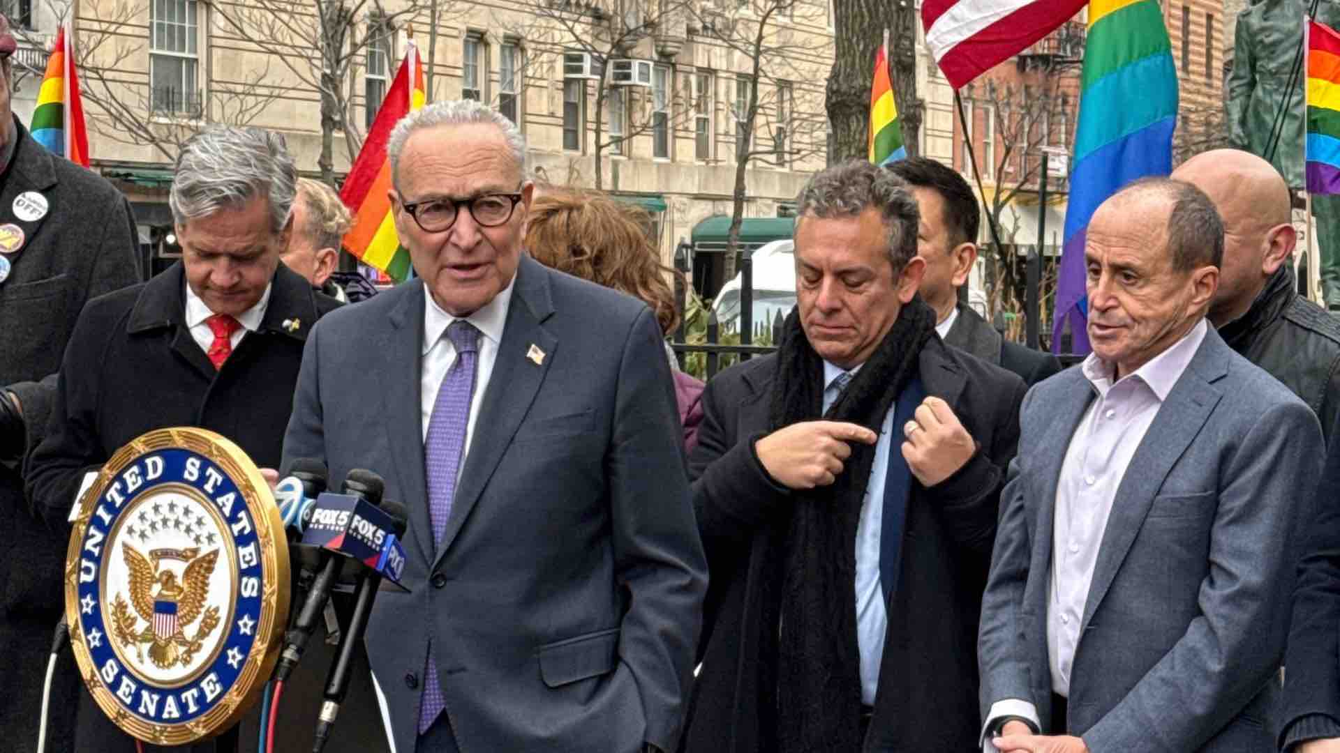 Senator Chuck Schumer at the Stonewall National Monument with Pride flags waving in the background