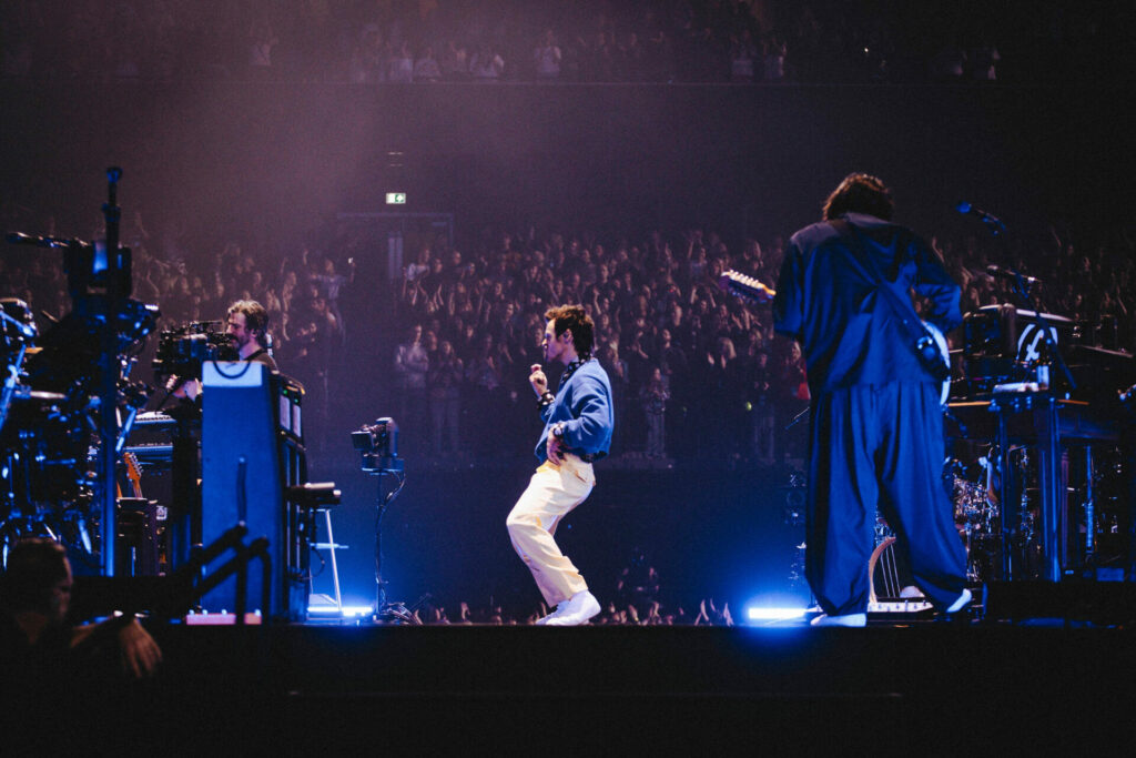 harry on stage bending his knees surrounded by crew members