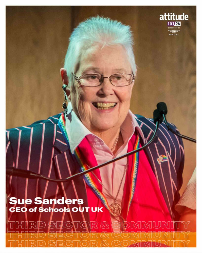 A portrait of Sue Sanders laughing at a microphone, wearing a navy blue pinstripe blazer over a pink shirt, with a rainbow lanyard, drop earrings and short white hair. The image is overlaid with Attitude 101 2026 branding and text identifying her as chief executive officer of Schools OUT UK in the Third Sector & Community category, empowered by Bentley.