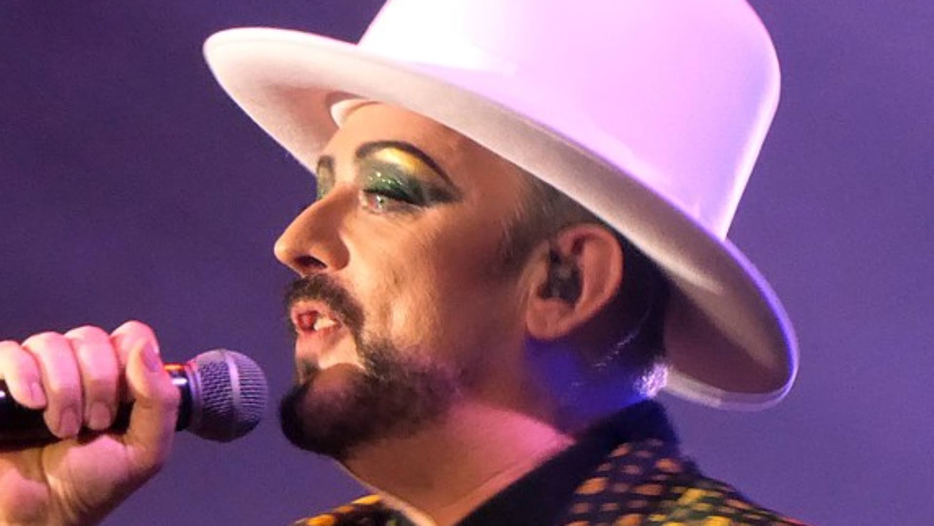 Boy George wearing a white hat singing into a microphone