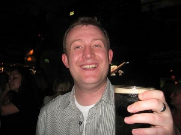 A smiling man holding up a pint of Guinness