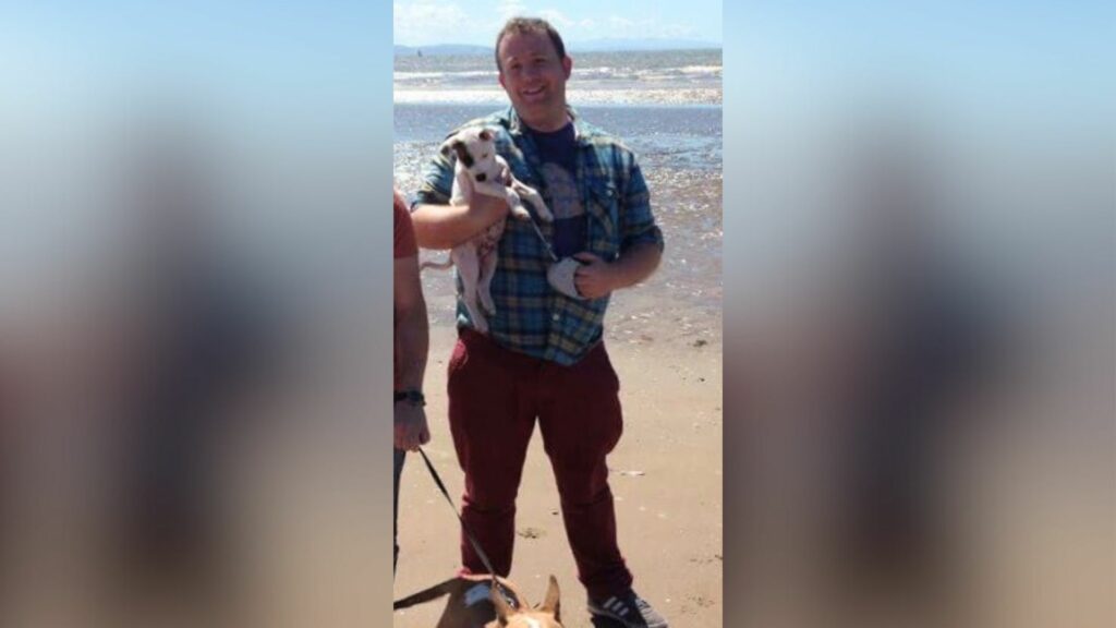 A man standing on a beach holding a dog