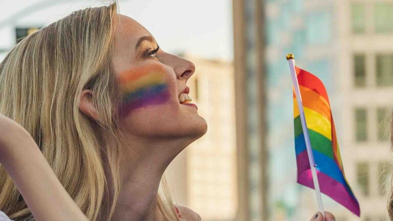 A woman with a pride flag painted across her check waving a Pride flag