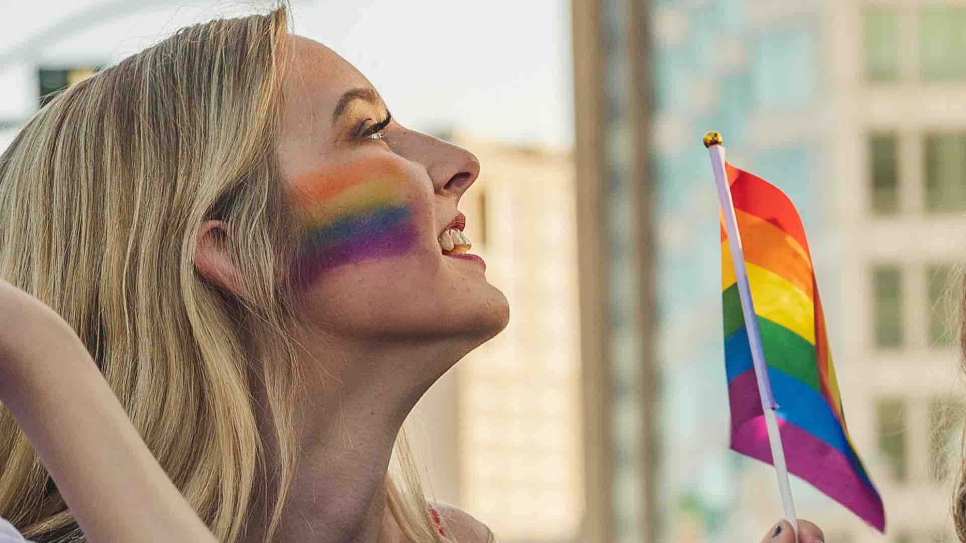 A woman with a pride flag painted across her check waving a Pride flag
