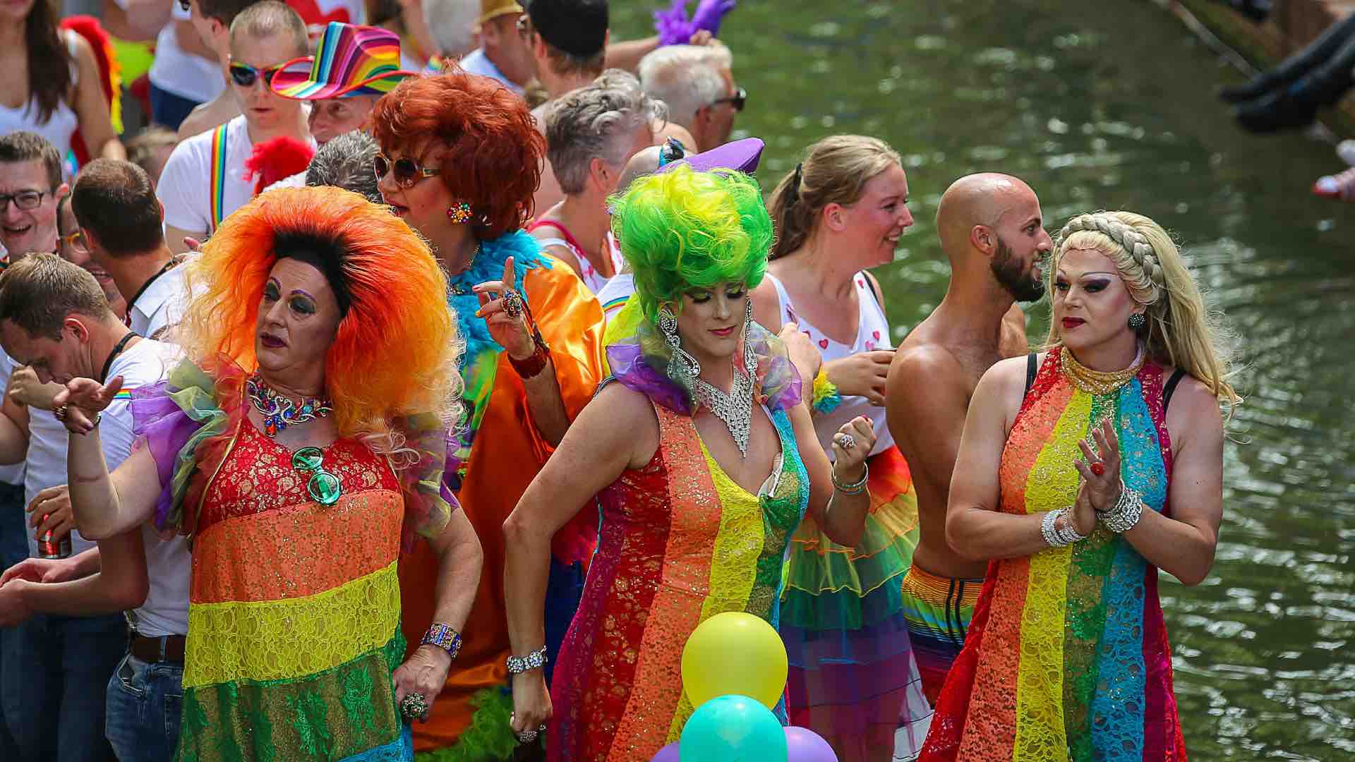 Drag queens in a Pride parade along a river bank