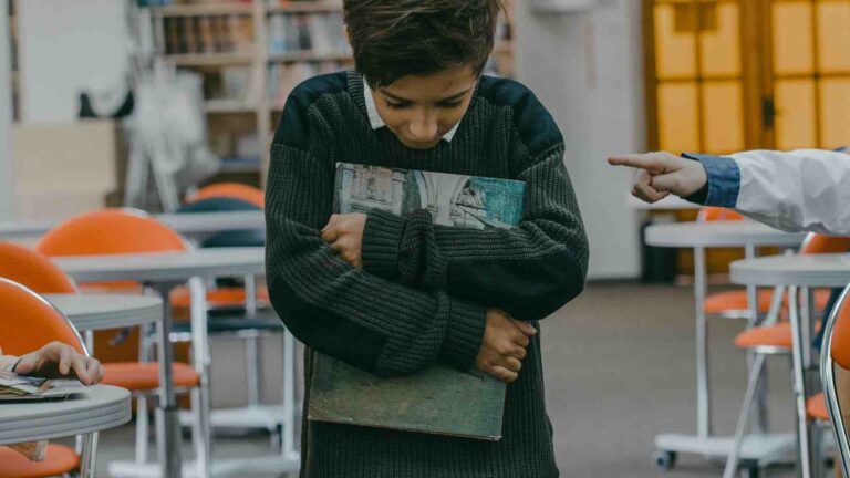 School boy holding a book looking down at the floor