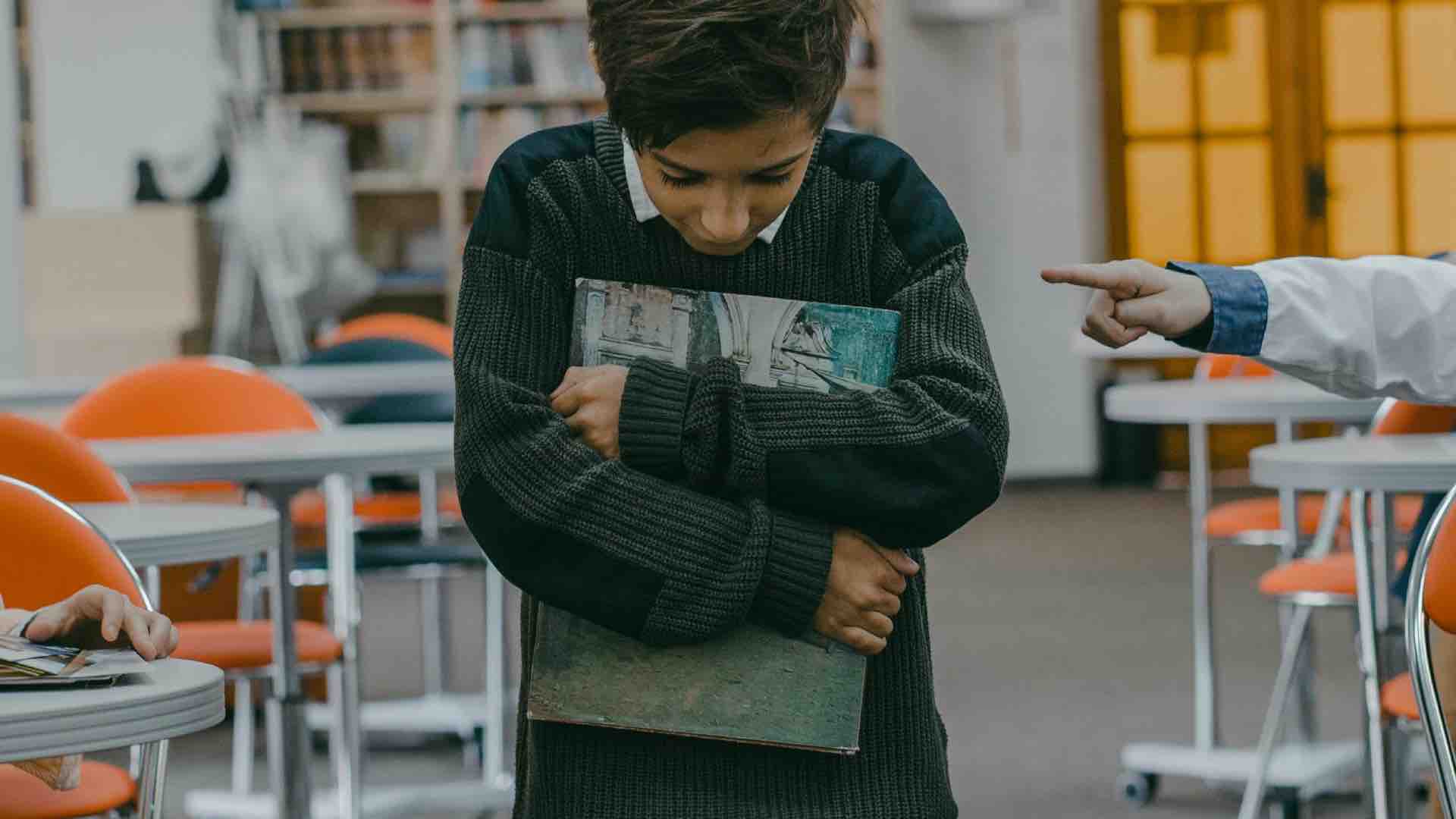 School boy holding a book looking down at the floor