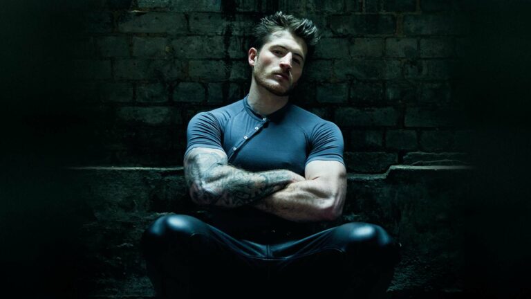 Kieron Moore in his attitude shoot in grey t-shirt, leather trousers sitting down(Image: Attitude/Bartek Szmigulski)