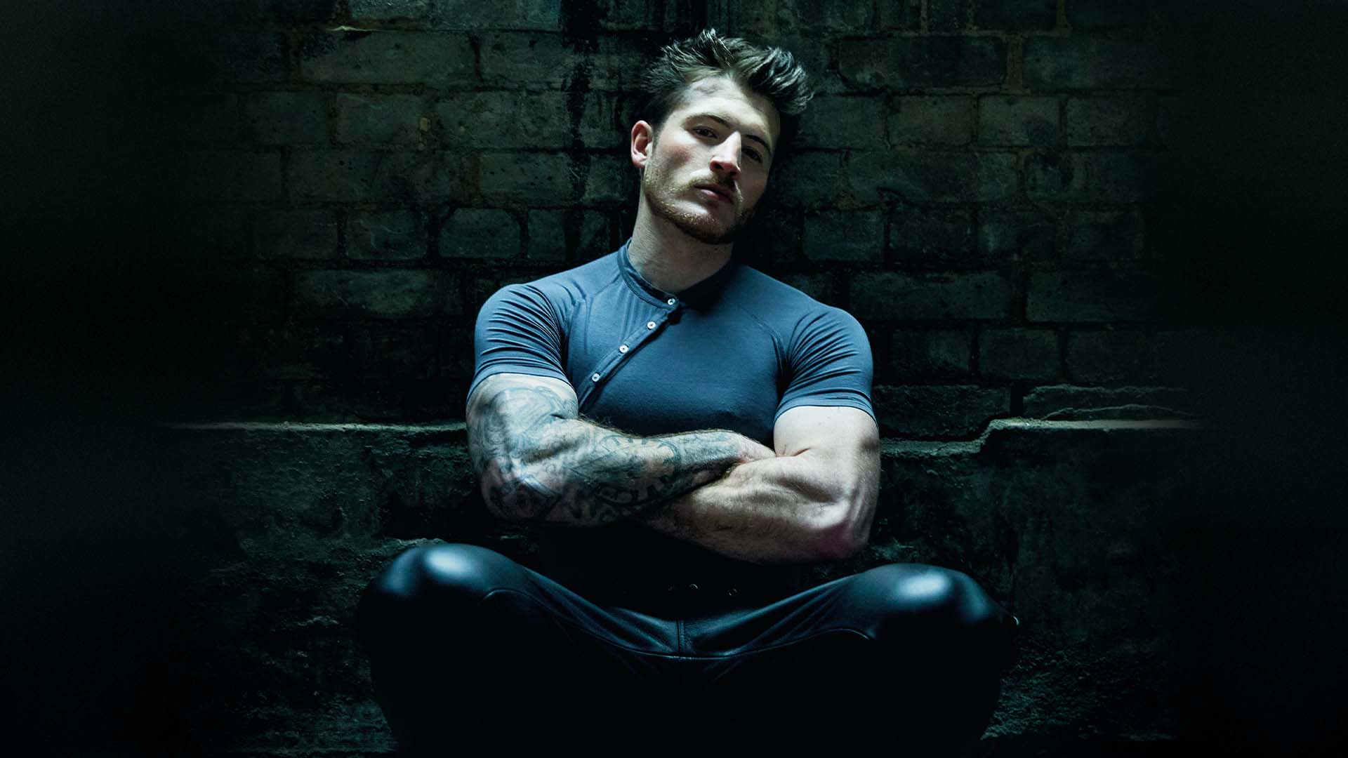 Kieron Moore in his attitude shoot in grey t-shirt, leather trousers sitting down(Image: Attitude/Bartek Szmigulski)