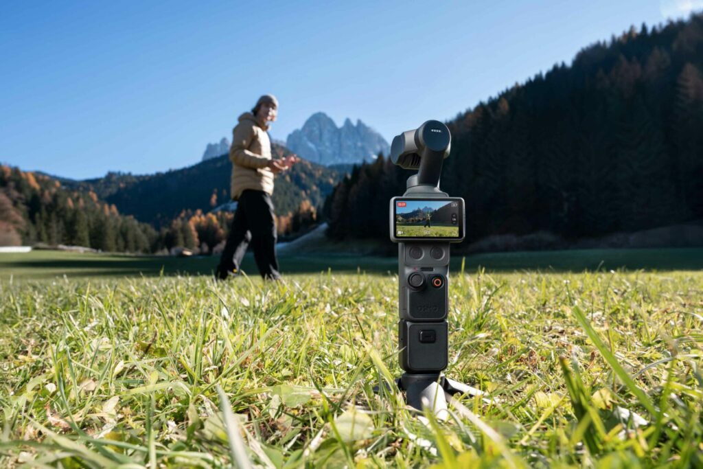 The DJI Osmo Pocket 4 positioned in a field tracking and filming its owner from a distance