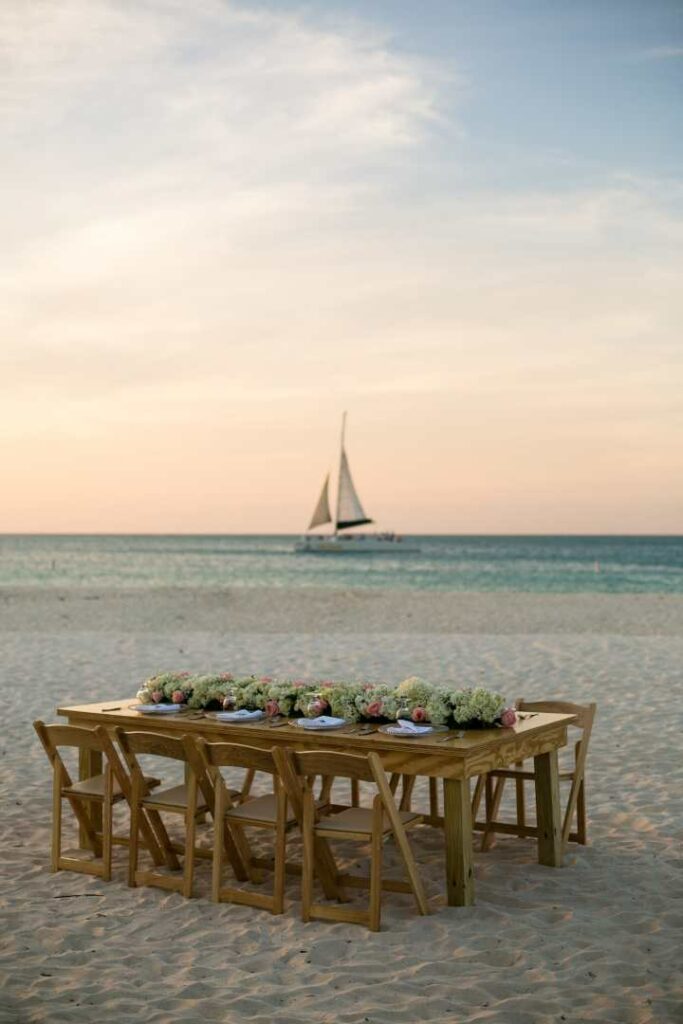 A dining table on a beach in Aruba with the ocean and a yacht in the background