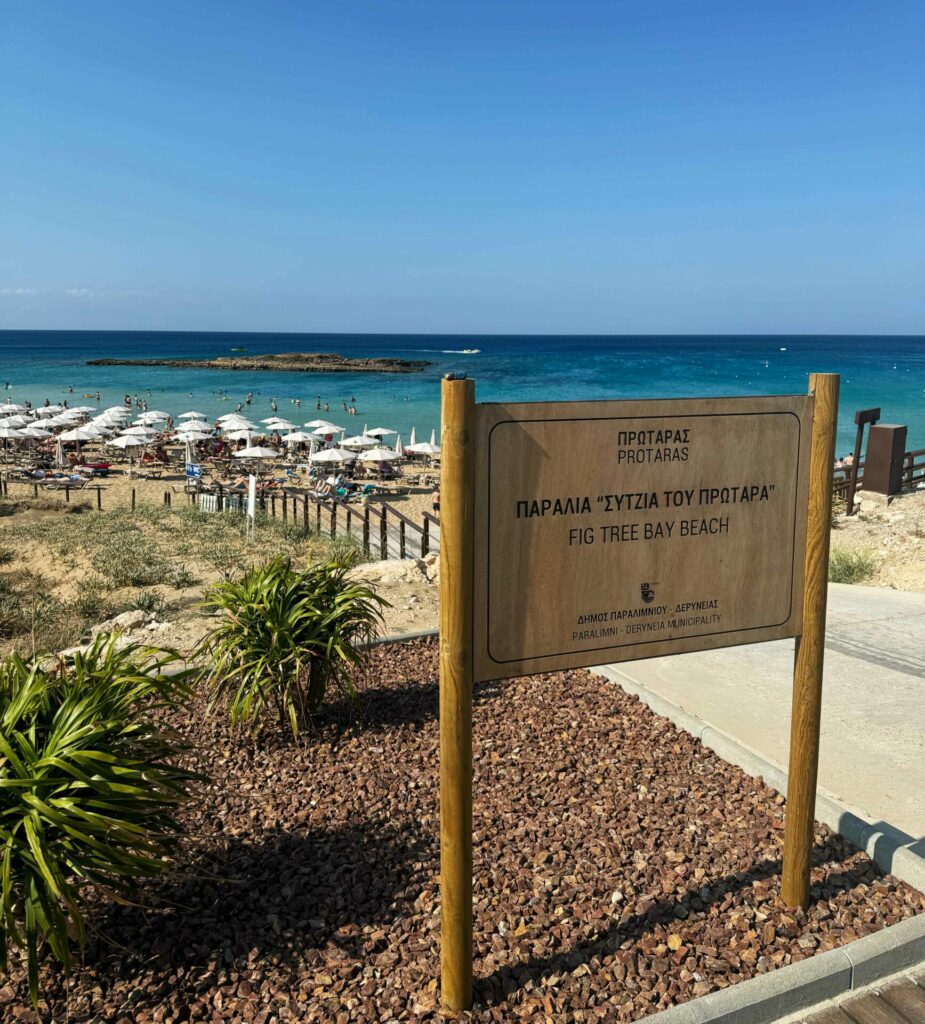 A sign for Fig Tree Bay with the beach beyond 