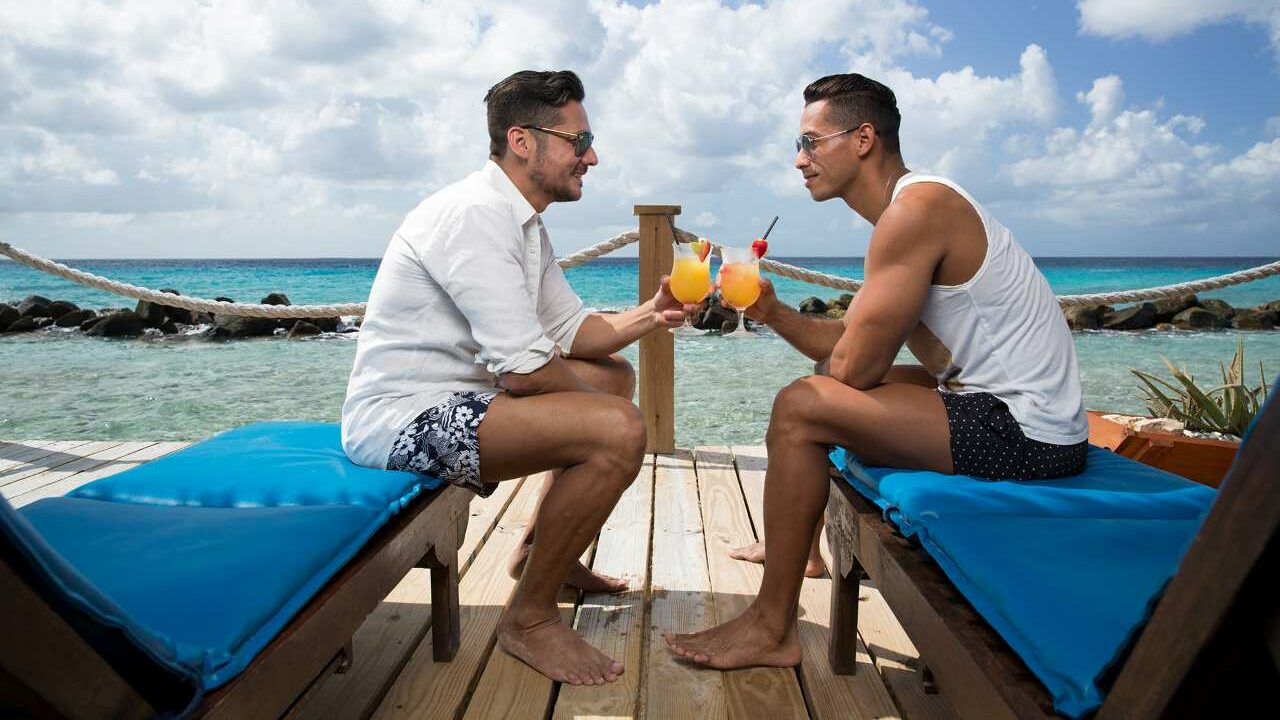 A gay couple on a beach in Aruba drinking cocktails