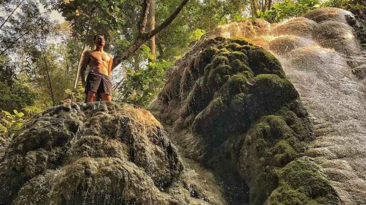 A shirtless man stands on the Bua Tong waterfall in Sri Lanna National Park
