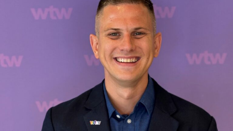 A smiling man standing in front of a purple photo board with the WTW logo on it