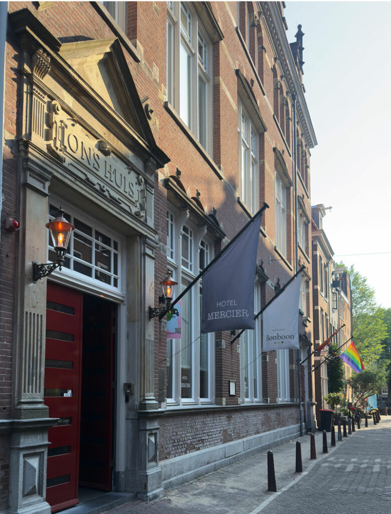 The exterior of Hotel Mercier, a brick building with flags with the hotel's name, the restaurant's name and a rainbow flag outside