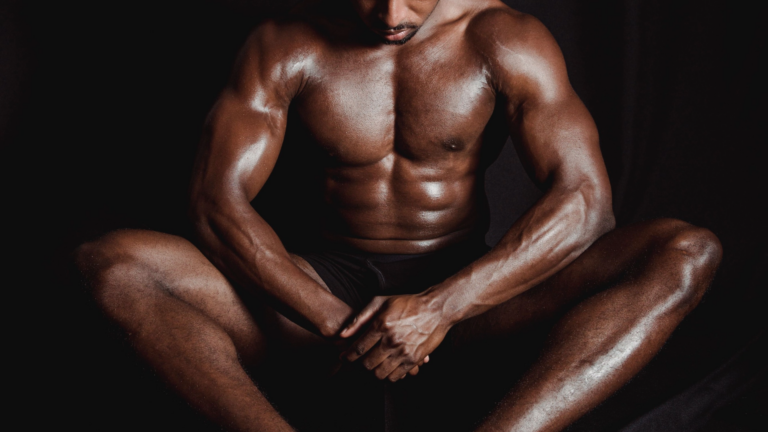 Shirtless bodybuilder sitting against a dark backdrop