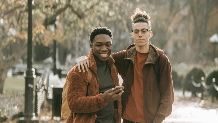 Two men standing side by side embracing and looking into the camera in an autumnal park scene