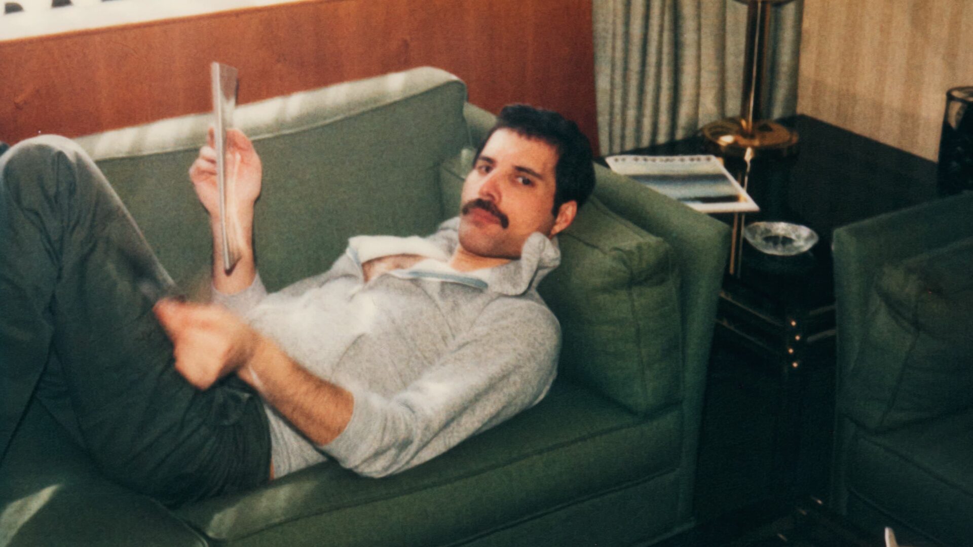 Freddie in a grey top lying on a green sofa and looking at the camera