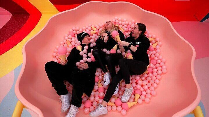 Three adults having fun amongst pink balls at the Ice Cream Museum